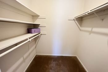 A walk in closet with white shelves and a purple box on a shelf